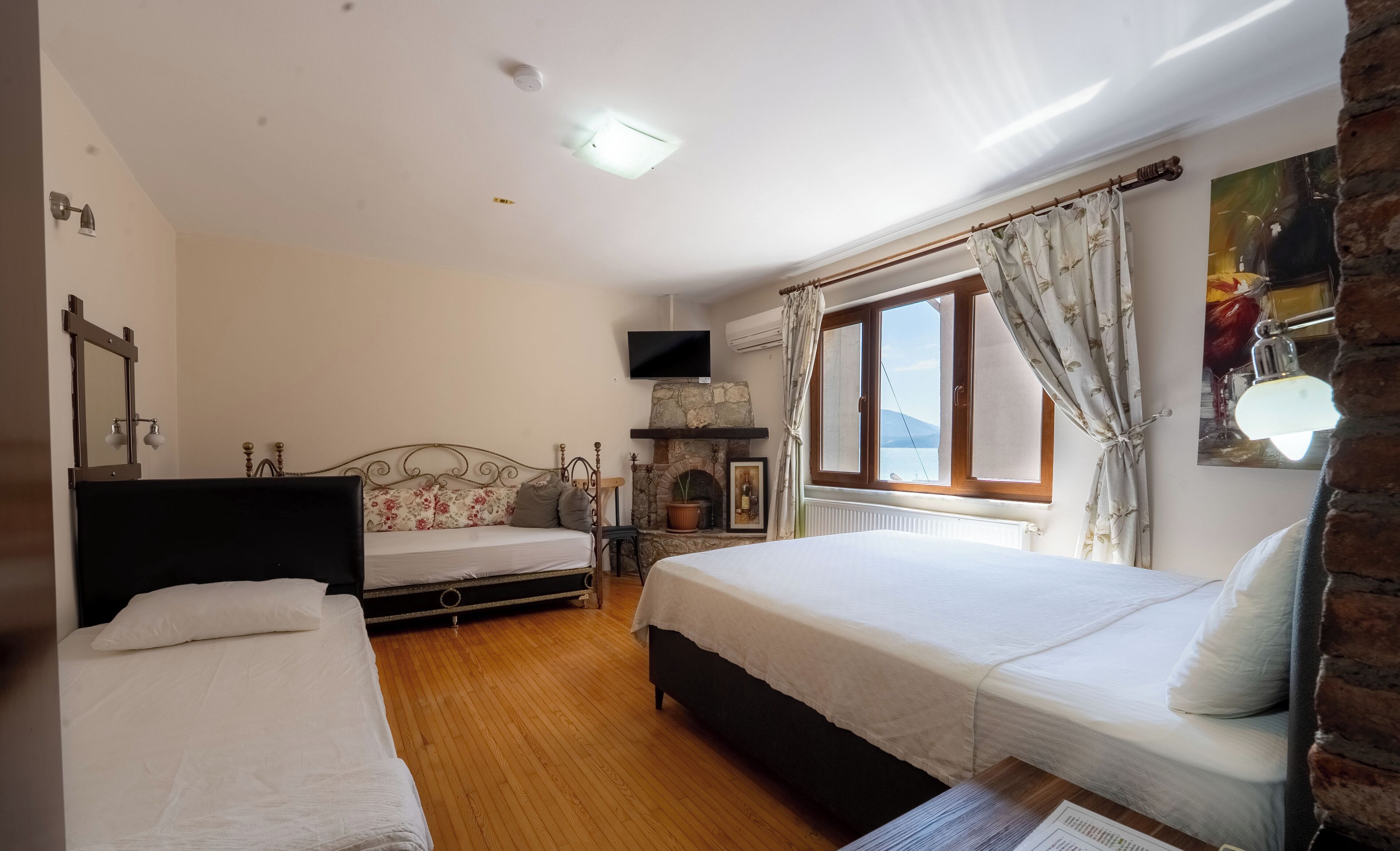 A bedroom with two beds, a stone fireplace, a television, and a window with curtains.