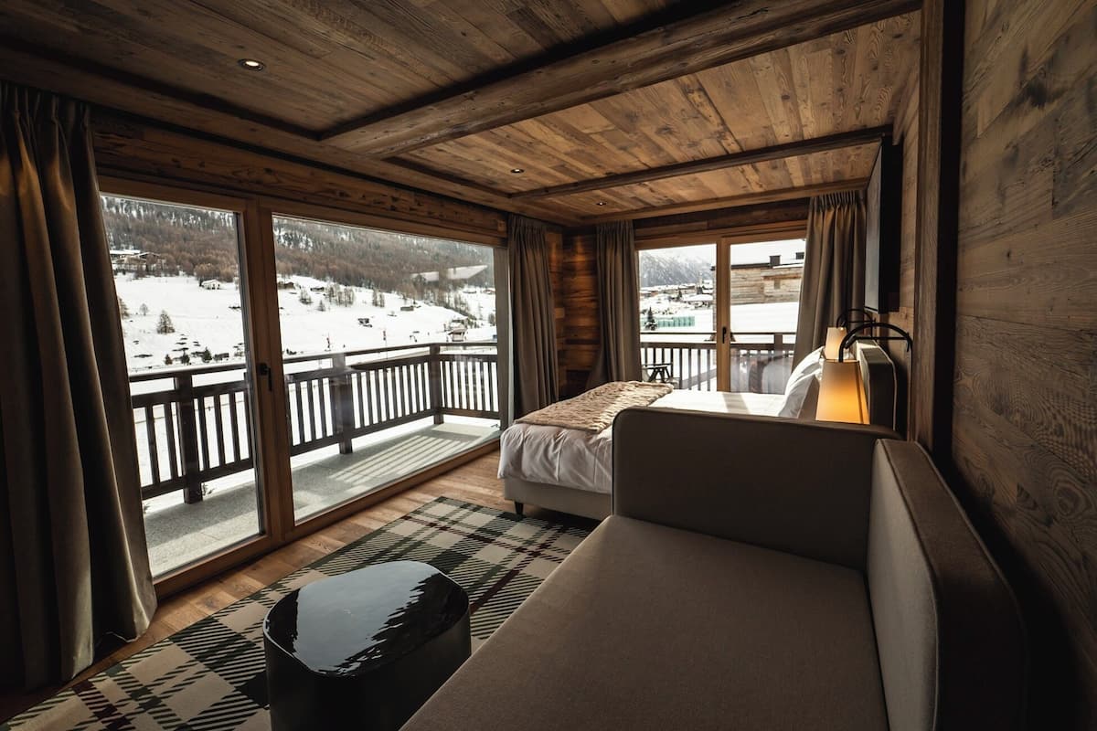 Habitación de hotel con cama, mesita de noche y vistas a un paisaje nevado.