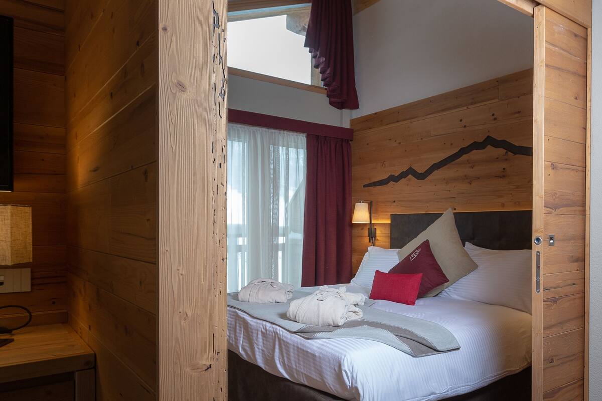 Una habitación de madera con una cama, un escritorio y una ventana con cortinas.