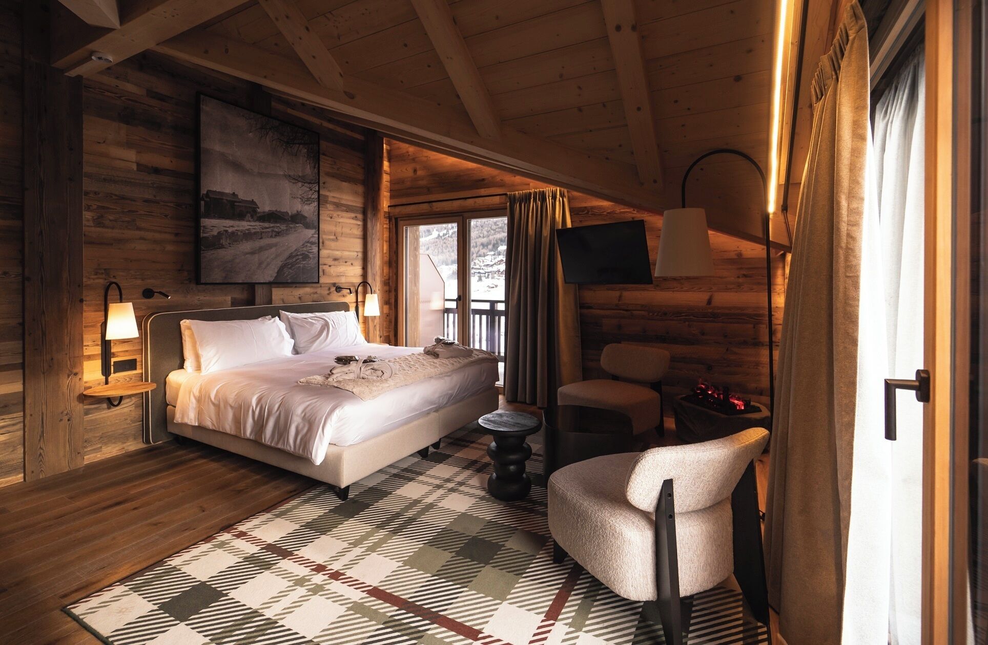 A cozy bedroom with a large bed, a chair, a TV, and a fireplace.