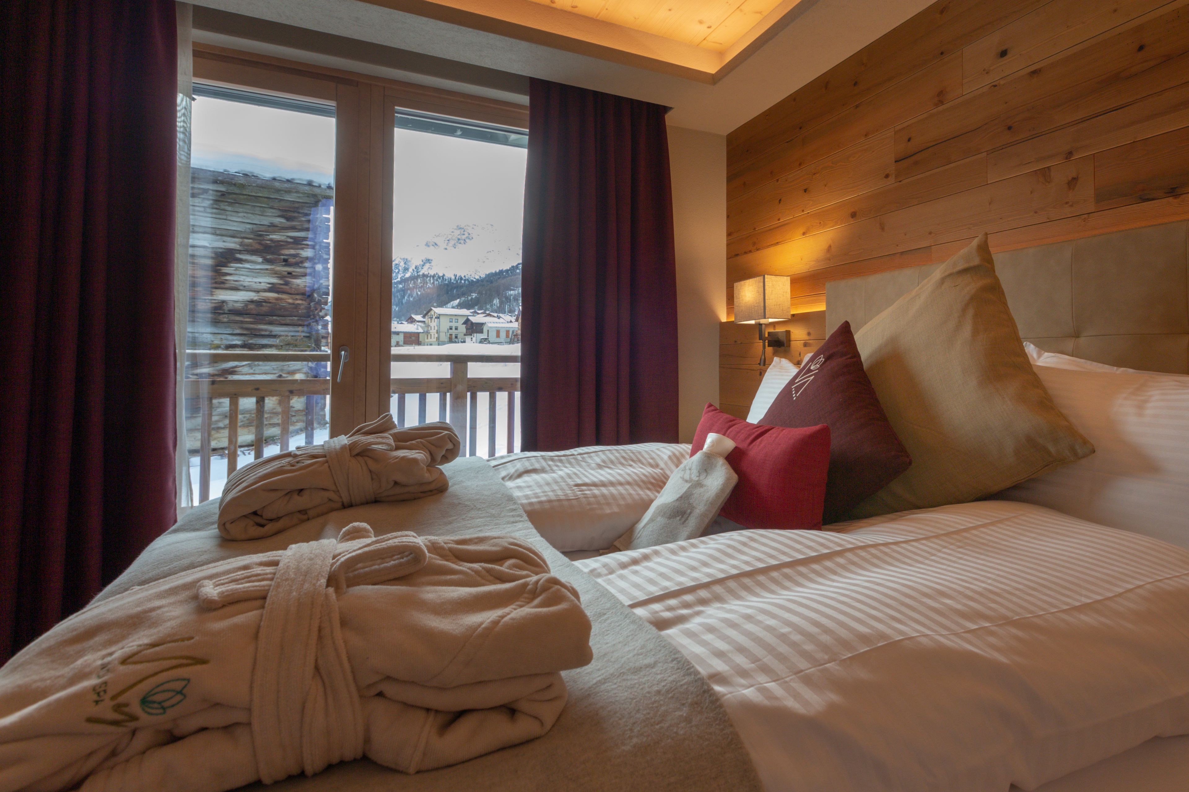 A hotel room with a large bed, two pillows, a headboard, and a window with curtains.
