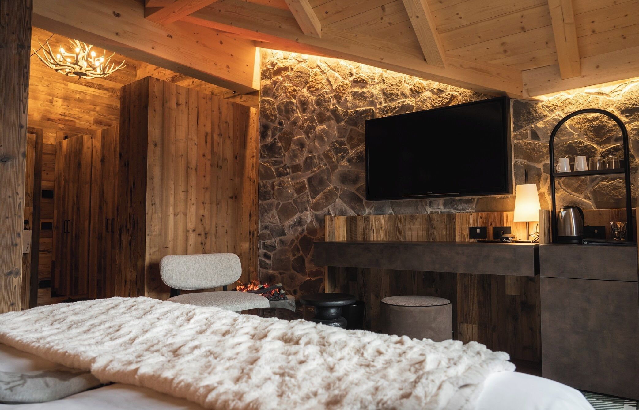 A cozy room with a stone wall, wooden ceiling, a flat-screen TV, a sofa, and a fireplace.