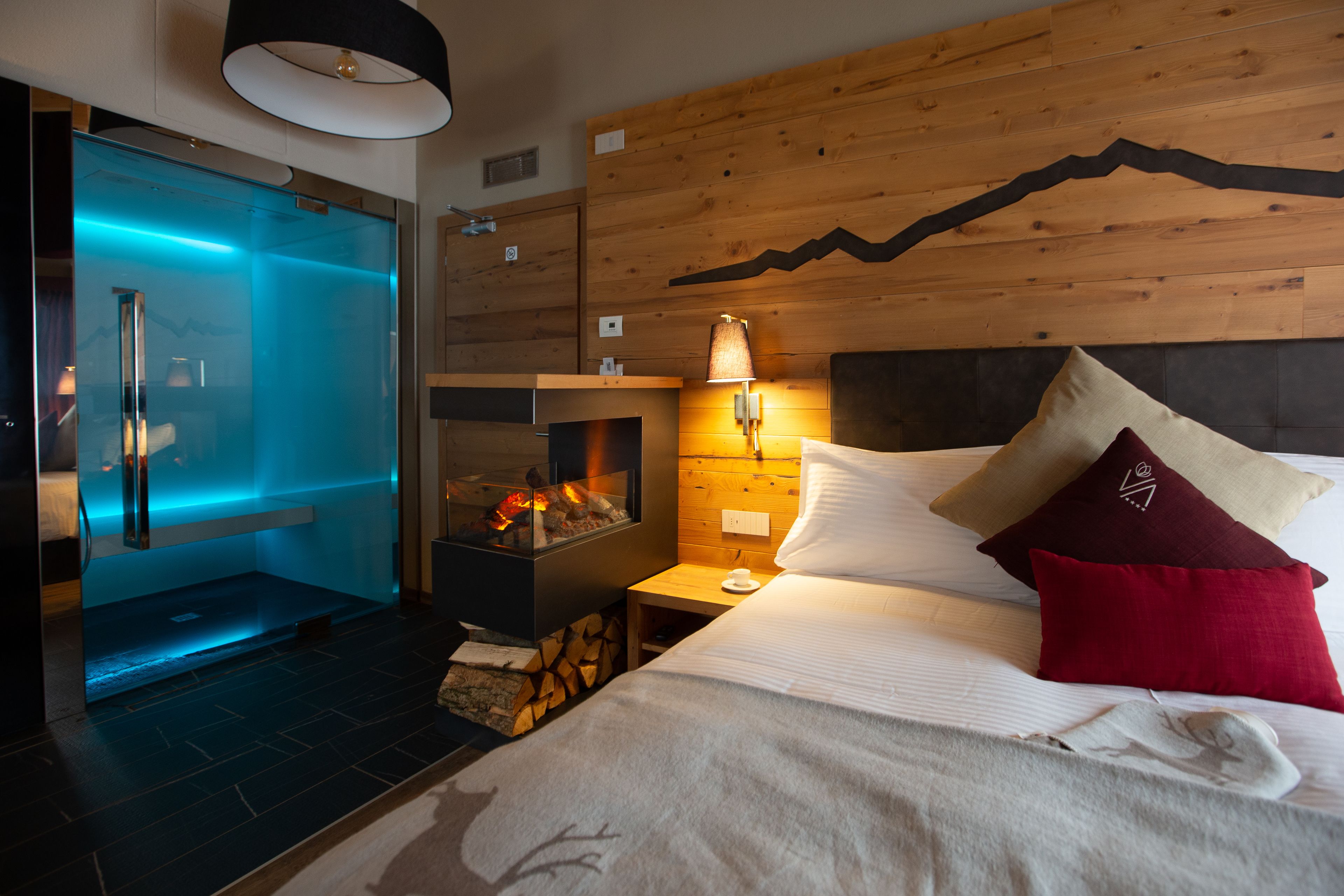 A modern hotel room with a glass-enclosed sauna, a wooden headboard, and a cozy bed with pillows.