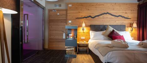 Una habitación de hotel moderna con un cabecero de madera, una cama con sábanas blancas, una mesita de noche con lámpara y una chimenea.
