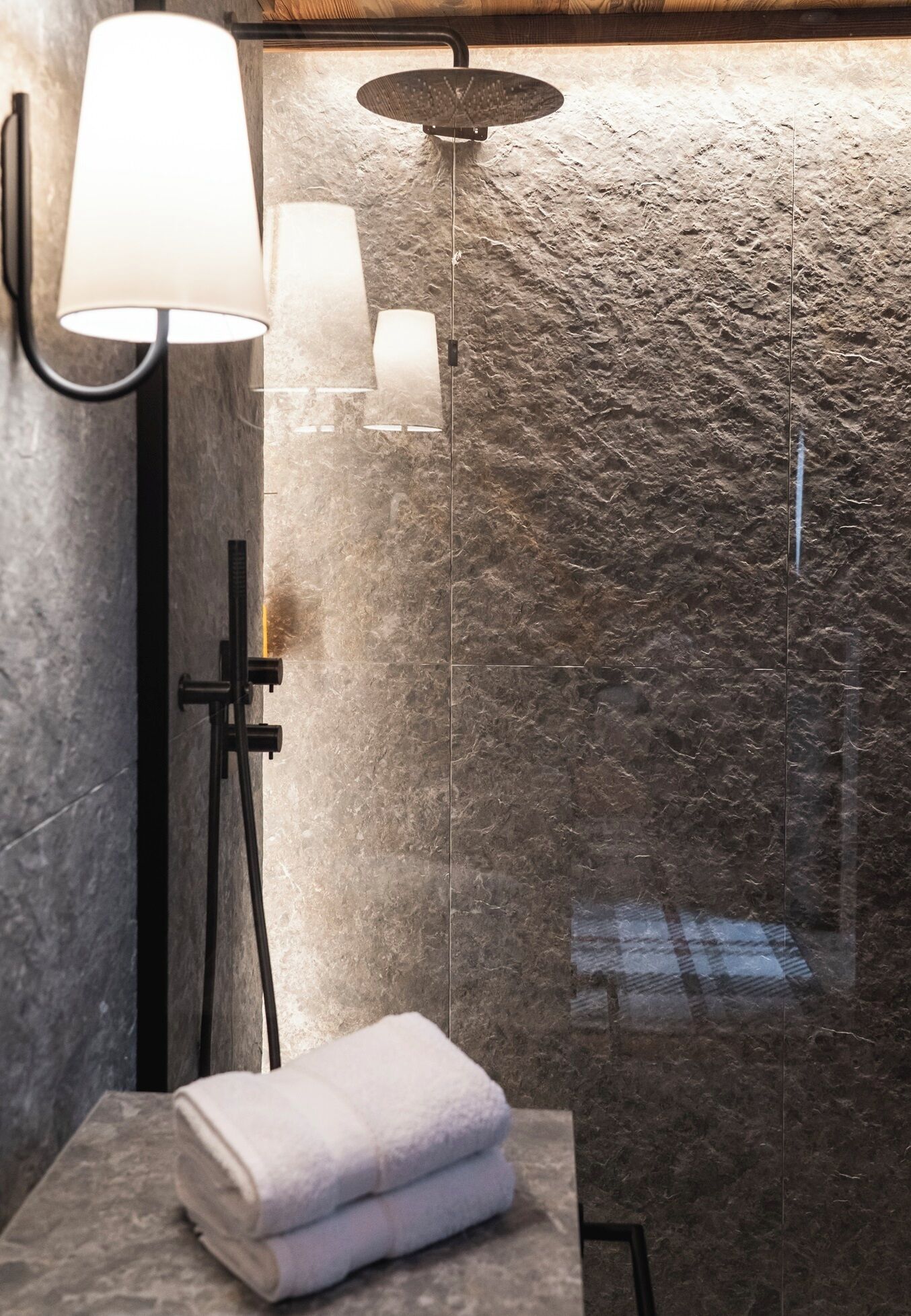 A modern bathroom with a stone-textured wall, a glass-enclosed shower, and a wall-mounted light fixture.
