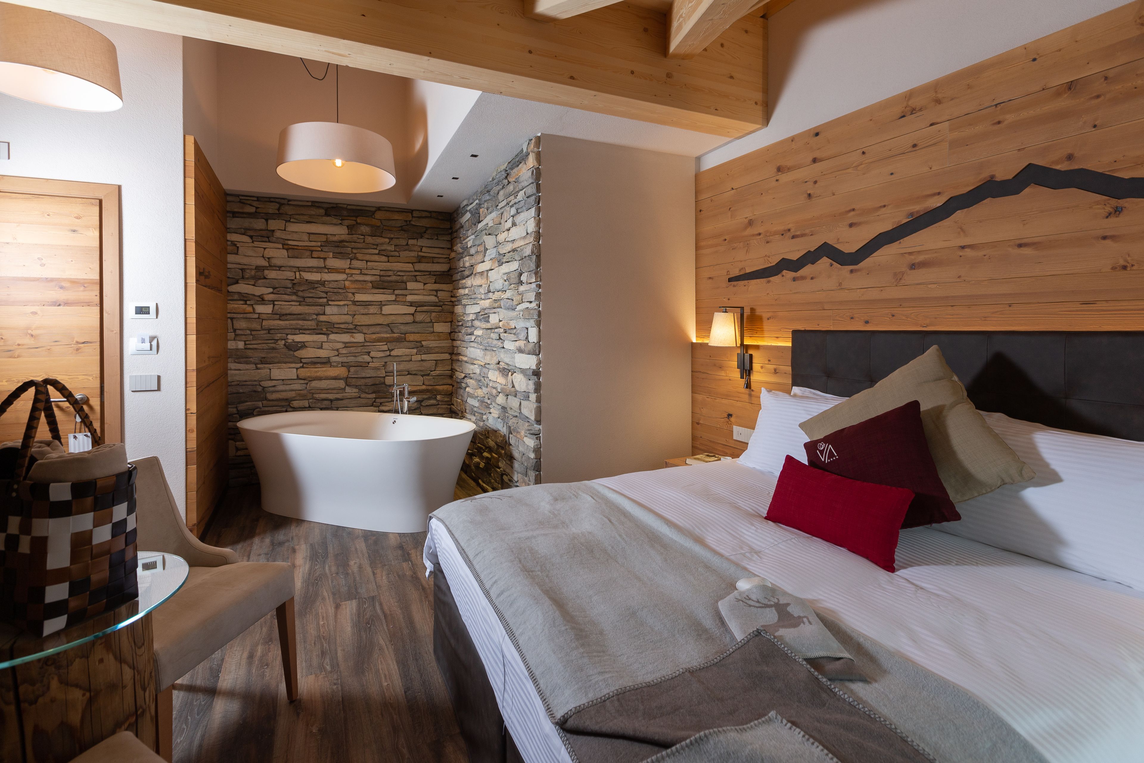 A modern bedroom with a large bed, a stone wall, and a wooden ceiling.