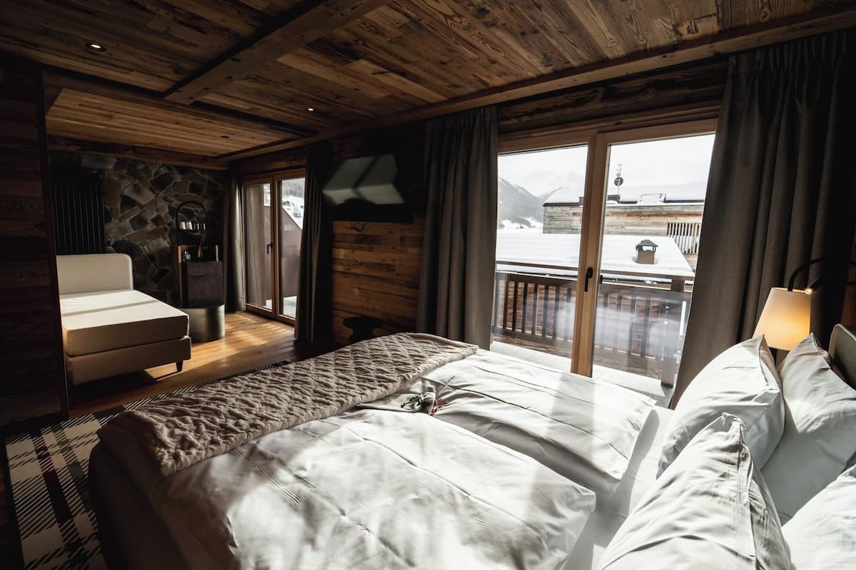 Un dormitorio acogedor con cama, una silla y un balcón con vistas a montañas.