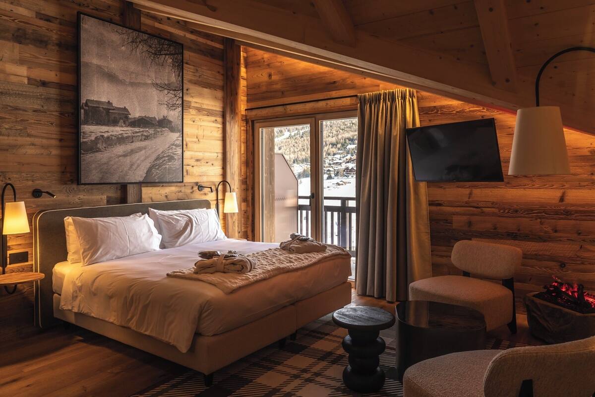 Una habitación acogedora con una cama, una silla, una mesita, un televisor y una chimenea.