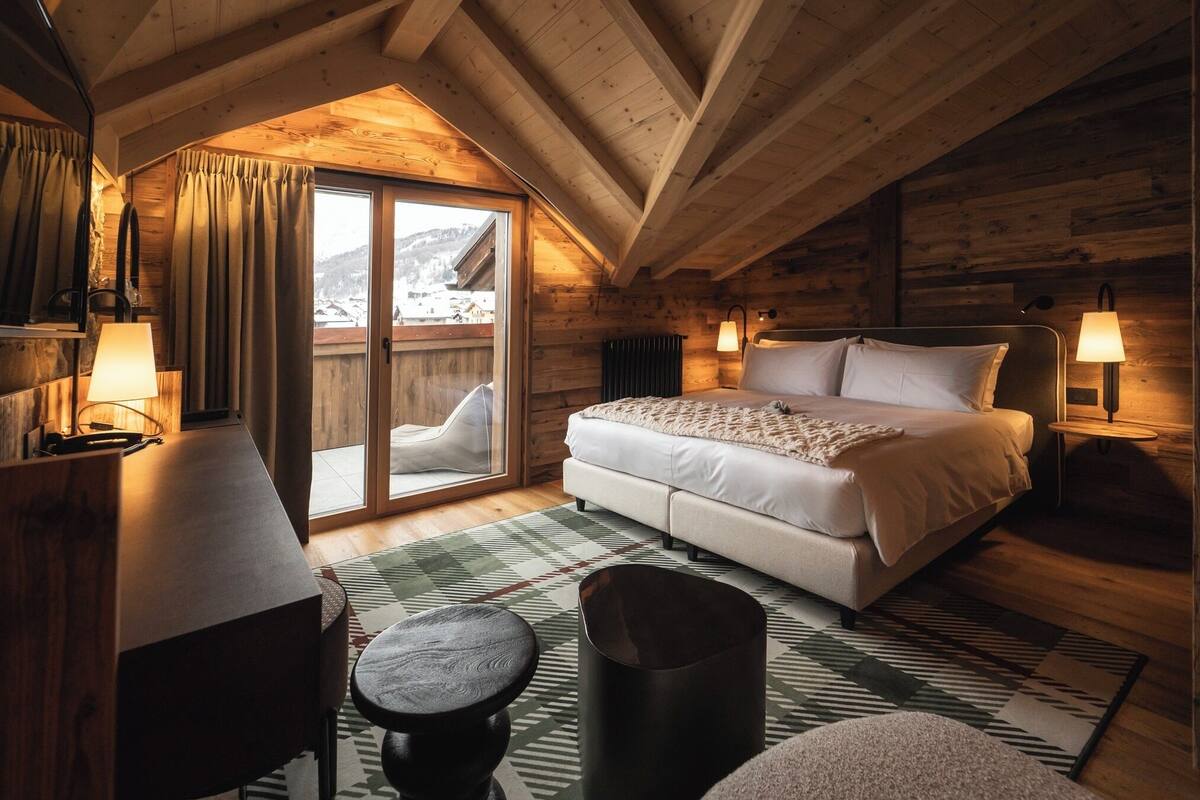 Un dormitorio acogedor con cama, lámparas de noche, un escritorio y vistas a un paisaje nevado a través de una puerta corrediza.