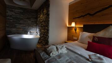 A modern bedroom with a stone wall, a large bathtub, a wooden headboard, and a neatly made bed with pillows.