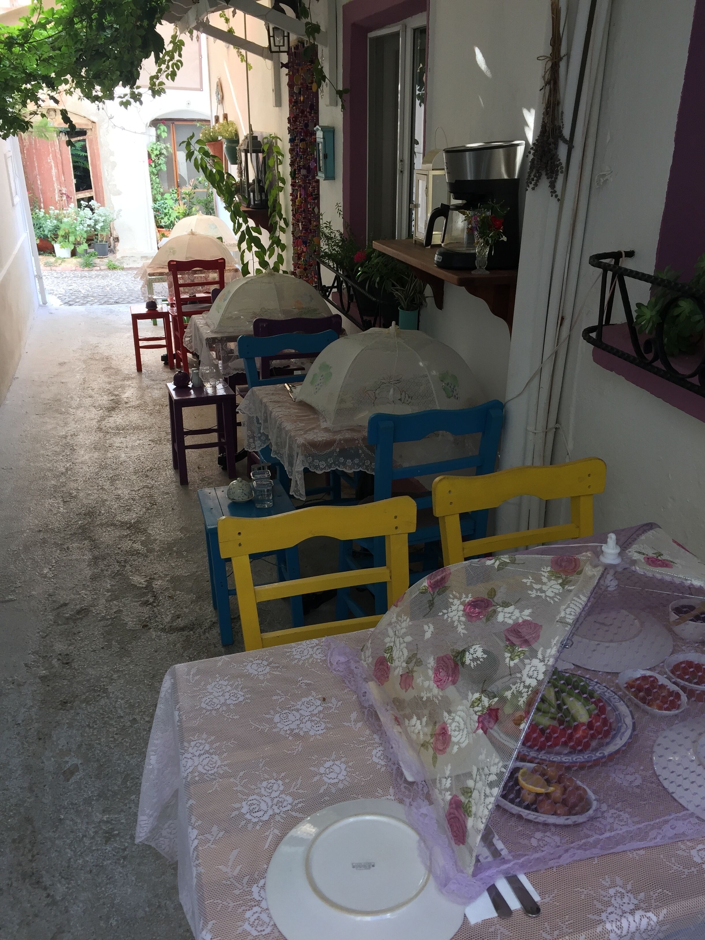 A patio with outdoor seating, including a table set for a meal, surrounded by chairs and covered with a floral tablecloth.