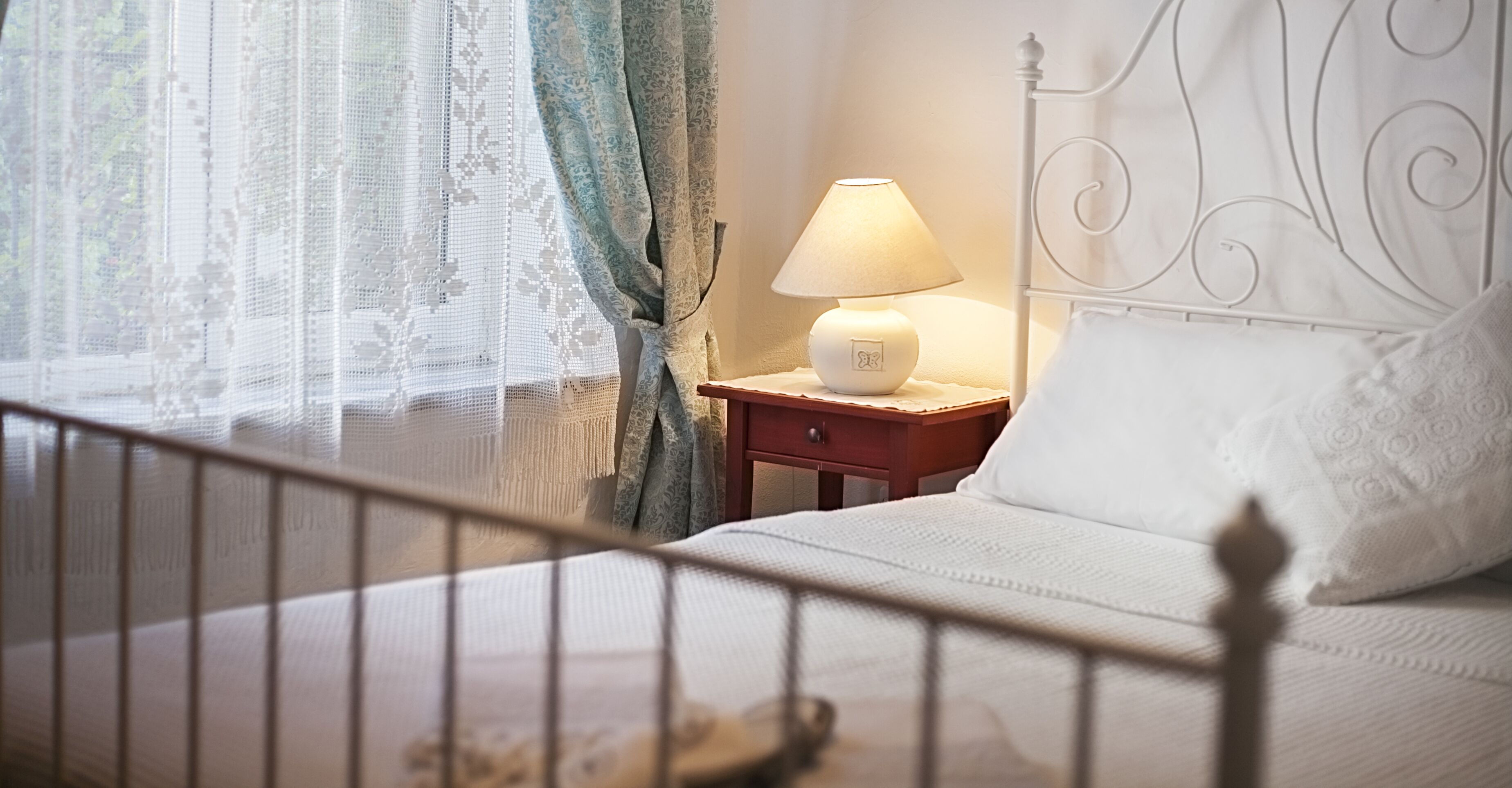 Een keurig opgemaakt bed met een wit kussen en een nachtkastje met een lamp.