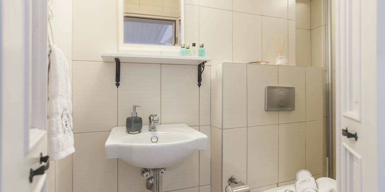 A bathroom with a white sink, a window above it, a towel hanging on the wall, and a shower area.