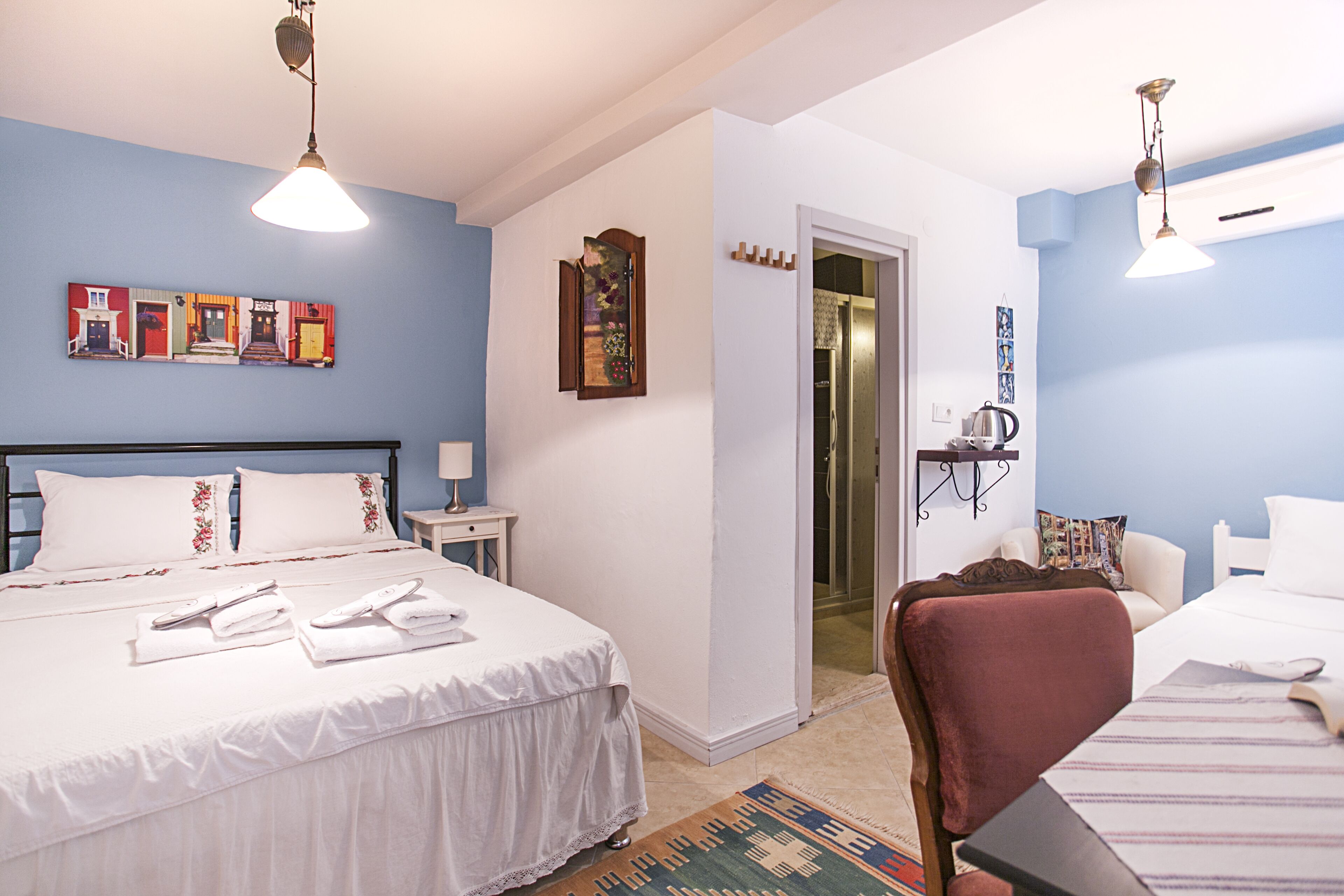 Una habitación de hotel con una cama, una silla, una mesita, una puerta y una pared decorada con obras de arte.