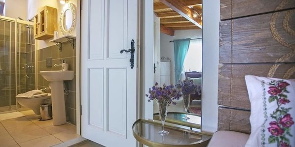 Une salle de bain avec une douche à parois de verre, un lavabo et des toilettes. Un miroir est placé au-dessus du lavabo et il y a une porte avec une poignée. Un vase rempli de fleurs est posé sur une petite table à côté de la porte.