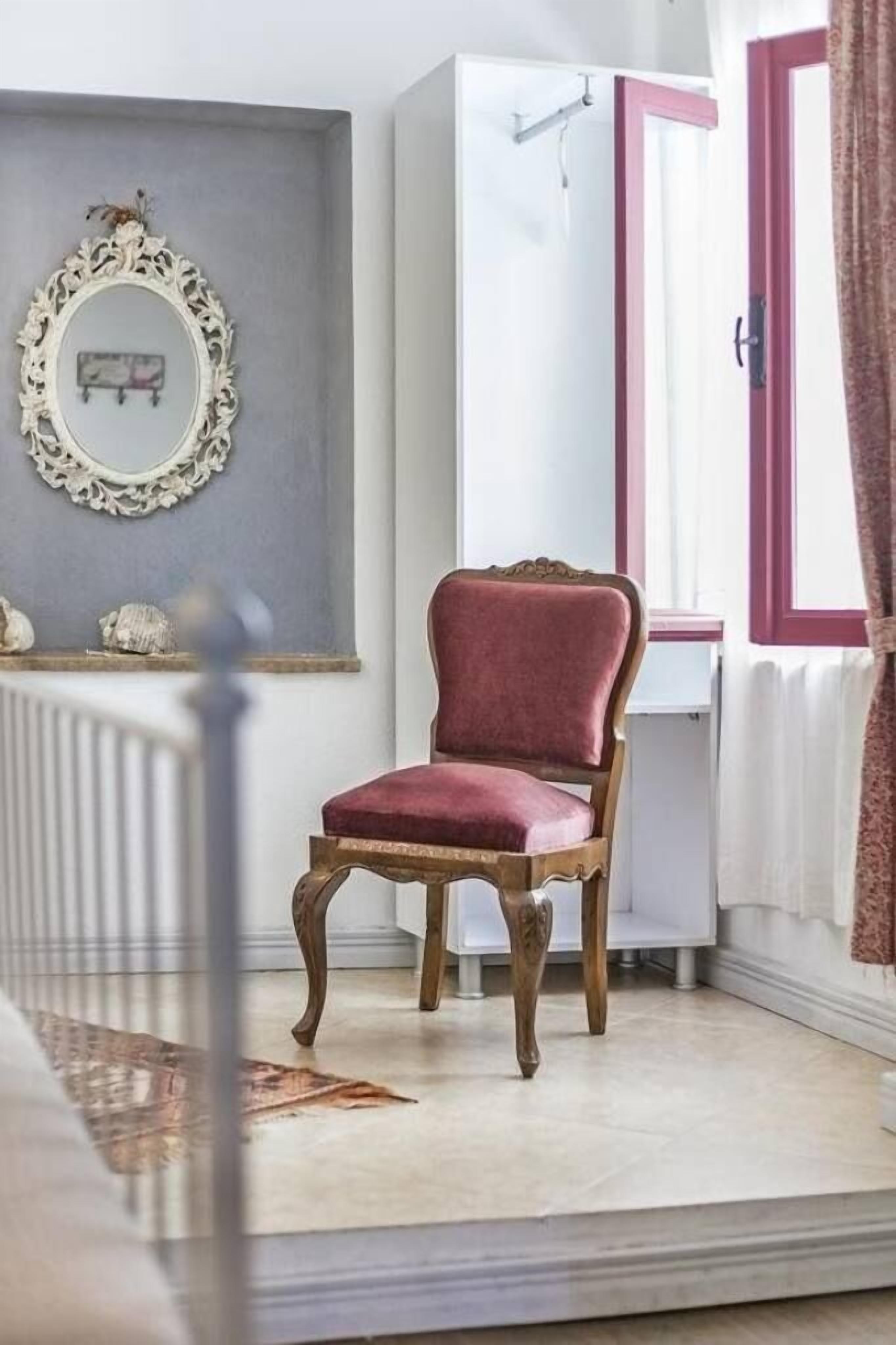 A room with a wooden chair, a white wardrobe, a mirror, and a window with curtains.