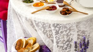 Une table dressée avec divers plats, notamment du pain, des salades et des boissons, sur une nappe blanche en dentelle.