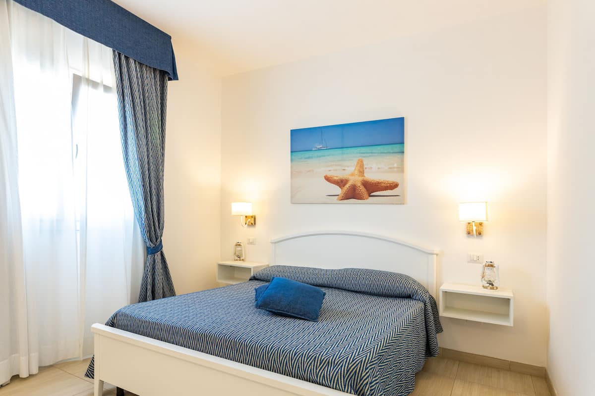 Una cama bien hecha con una colcha estampada, una decoración con forma de estrella de mar y un cuadro de una playa en la pared.