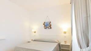 Una habitación de hotel con cama, mesitas de noche, una obra de arte en la pared y una cortina.