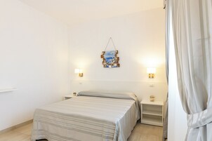 Una habitación de hotel con cama, mesitas de noche, una obra de arte en la pared y una cortina.