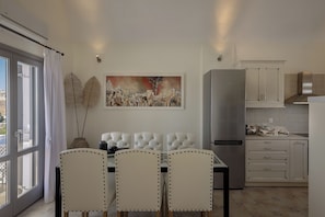 A modern kitchen with a refrigerator, cabinets, and a dining area with chairs.