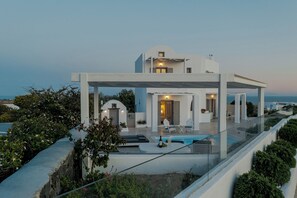 A modern villa with a pool, outdoor seating, and a view of the sea.