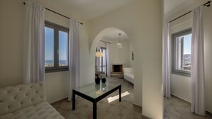 A living room with a sofa, a glass-top table, a fireplace, and large windows with curtains. - Hemera Holiday Home (Santorini)