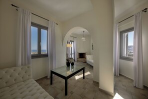 A living room with a sofa, a glass-top table, a fireplace, and large windows with curtains. - Hemera Holiday Home (Santorini)