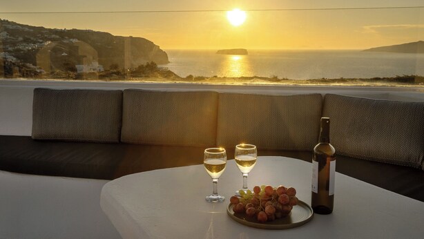 A table with two wine glasses, a bottle, and a plate of grapes. - Hemera Holiday Home (Santorini)
