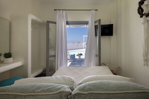 A hotel room with a bed, a TV, a small table with a drink, and a view of the pool and sky. - Hemera Holiday Home (Santorini)