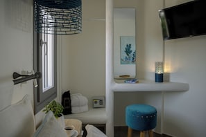 A modern bathroom with a shower, a towel rack, a small table with a cup, a plant, and a blue stool.