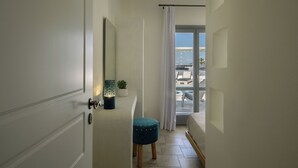 A narrow hallway with a door, a small stool, a potted plant, and a view of a pool area through a glass door. - Hemera Holiday Home (Santorini)