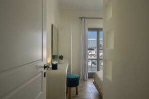 A narrow hallway with a door, a small stool, a potted plant, and a view of a pool area through a glass door. - Hemera Holiday Home (Santorini)