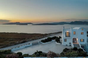 A white building with a balcony, a paved area, and a view of the sea and islands. - Hemera Holiday Home (Santorini)