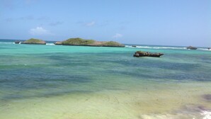 Une plage bordée d’une eau turquoise et limpide, de petites îles et d’un promontoire rocheux.