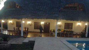 Un bâtiment à toit de chaume doté d’une piscine, d’un espace extérieur aménagé et d’une terrasse bien éclairée.