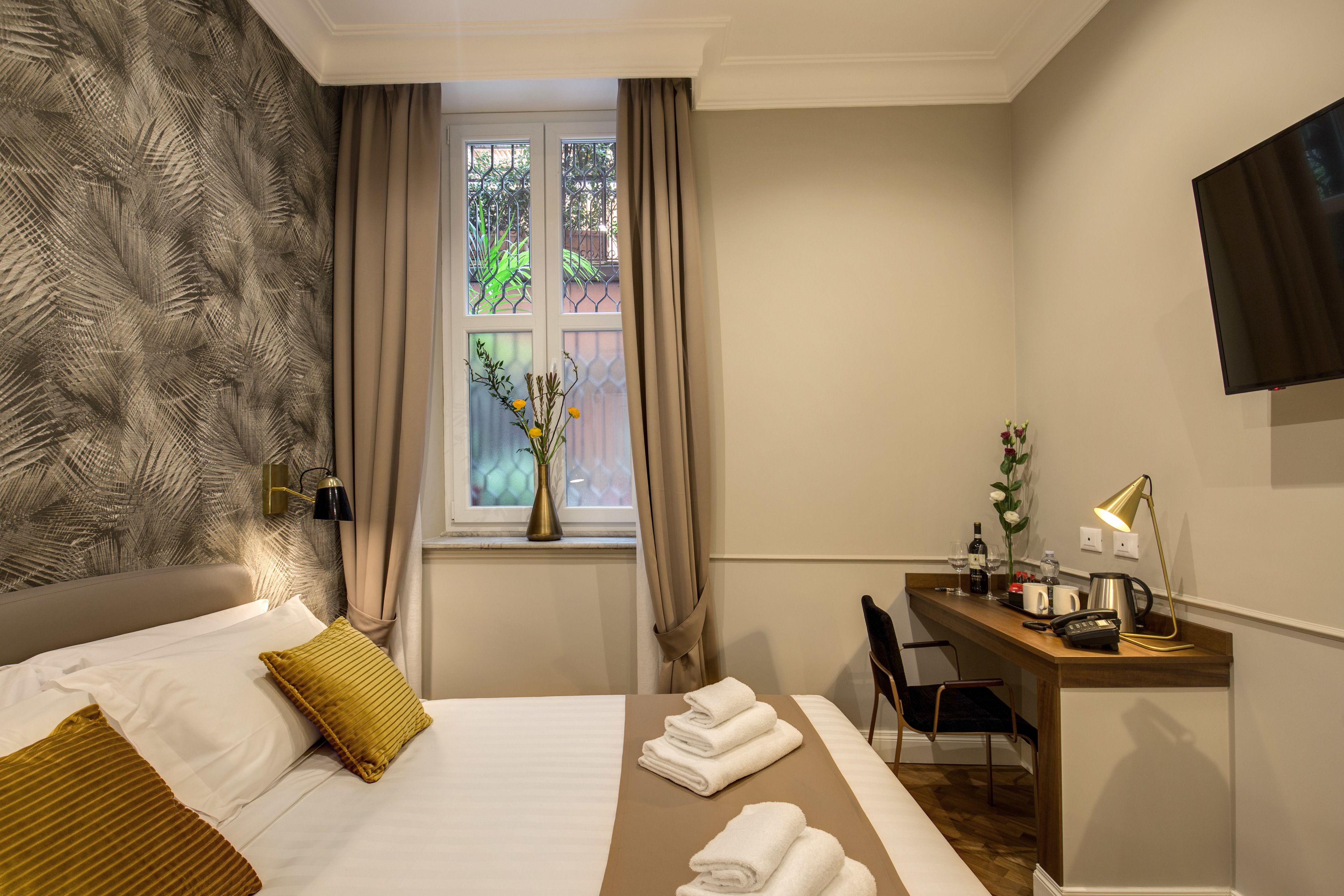 Une chambre d’hôtel avec un lit, un bureau, une chaise, une télévision et une fenêtre avec des rideaux.