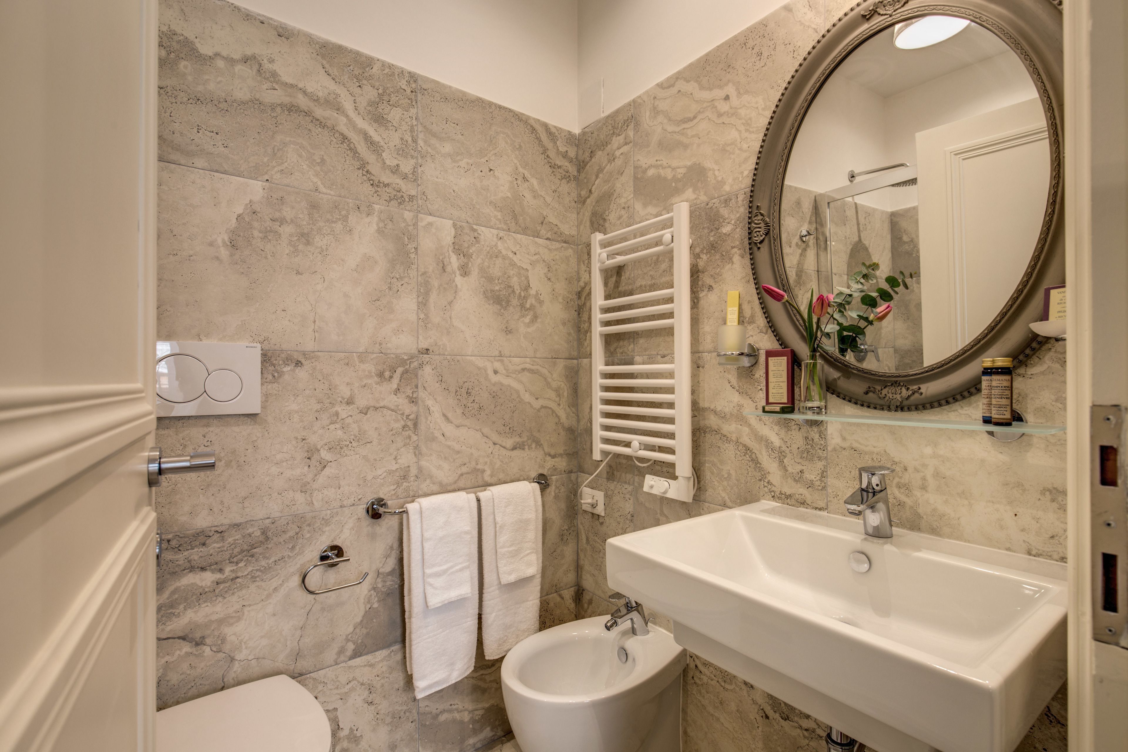 A bathroom with a marble wall, a white sink, a bidet, and a towel rack.