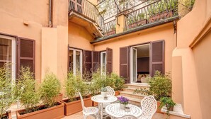 Een binnentuin met een tafel en stoelen, planten in potten, en een balkon met een balustrade.