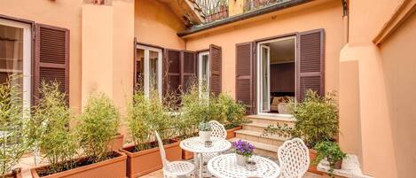 A courtyard with a table and chairs, potted plants, and a balcony with a railing.