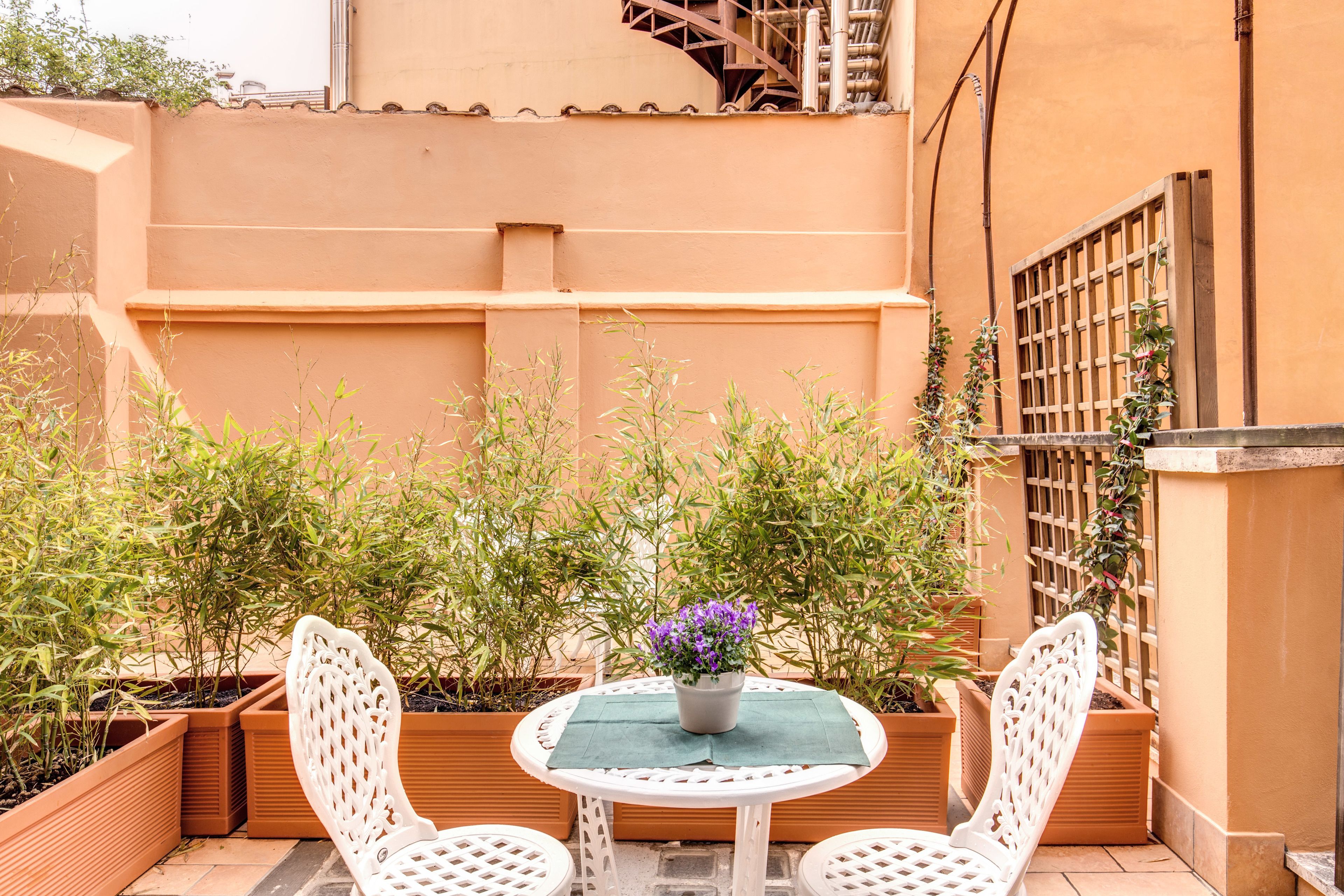 A small patio with two white chairs, a round table, and a potted plant with purple flowers.