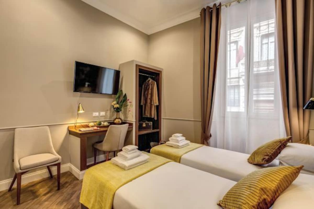 Habitación de hotel con dos camas, un escritorio, una silla, un televisor y un armario.