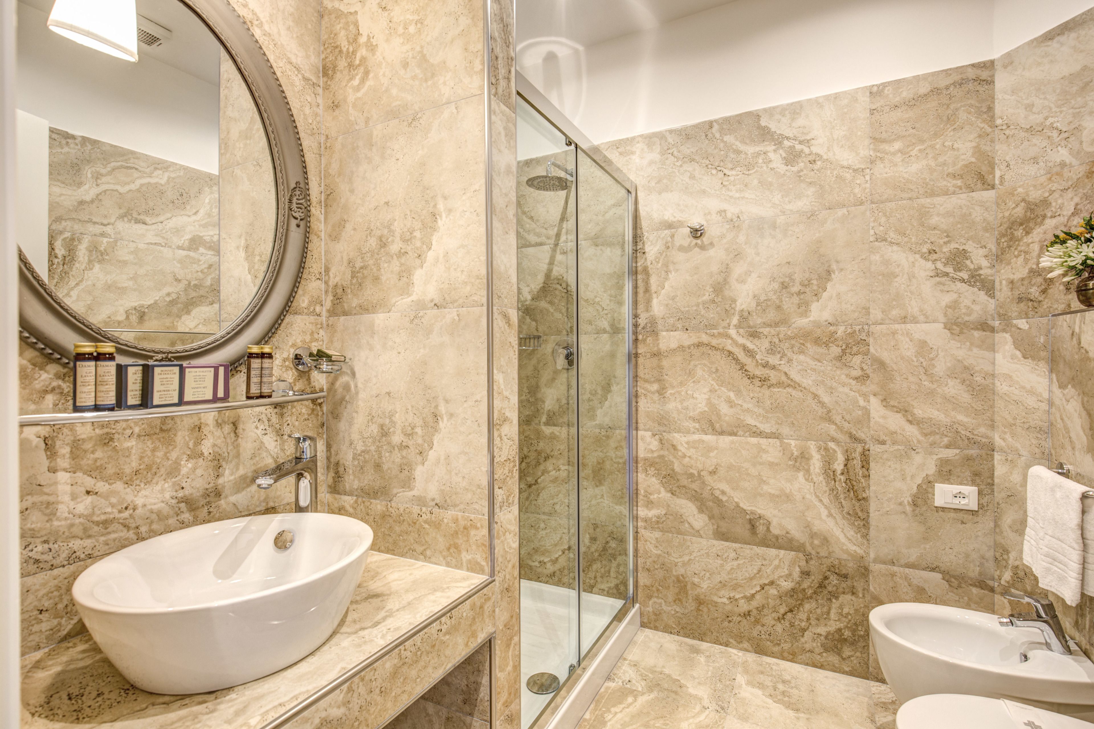 A bathroom with a large oval sink, a glass-enclosed shower, and a marble-tiled wall.