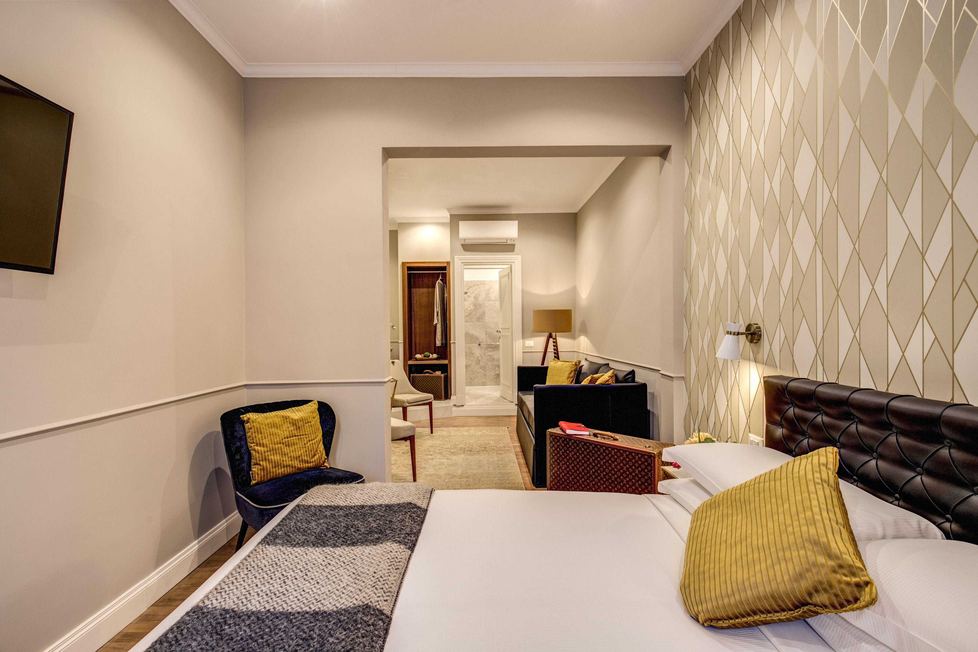 A hotel room with a bed, a chair, a desk, and a bathroom visible through an open door.