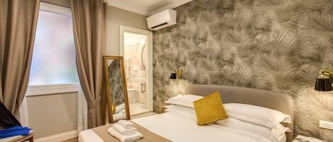 Habitación de hotel con cama, espejo, mesita de noche y ventana con cortinas.