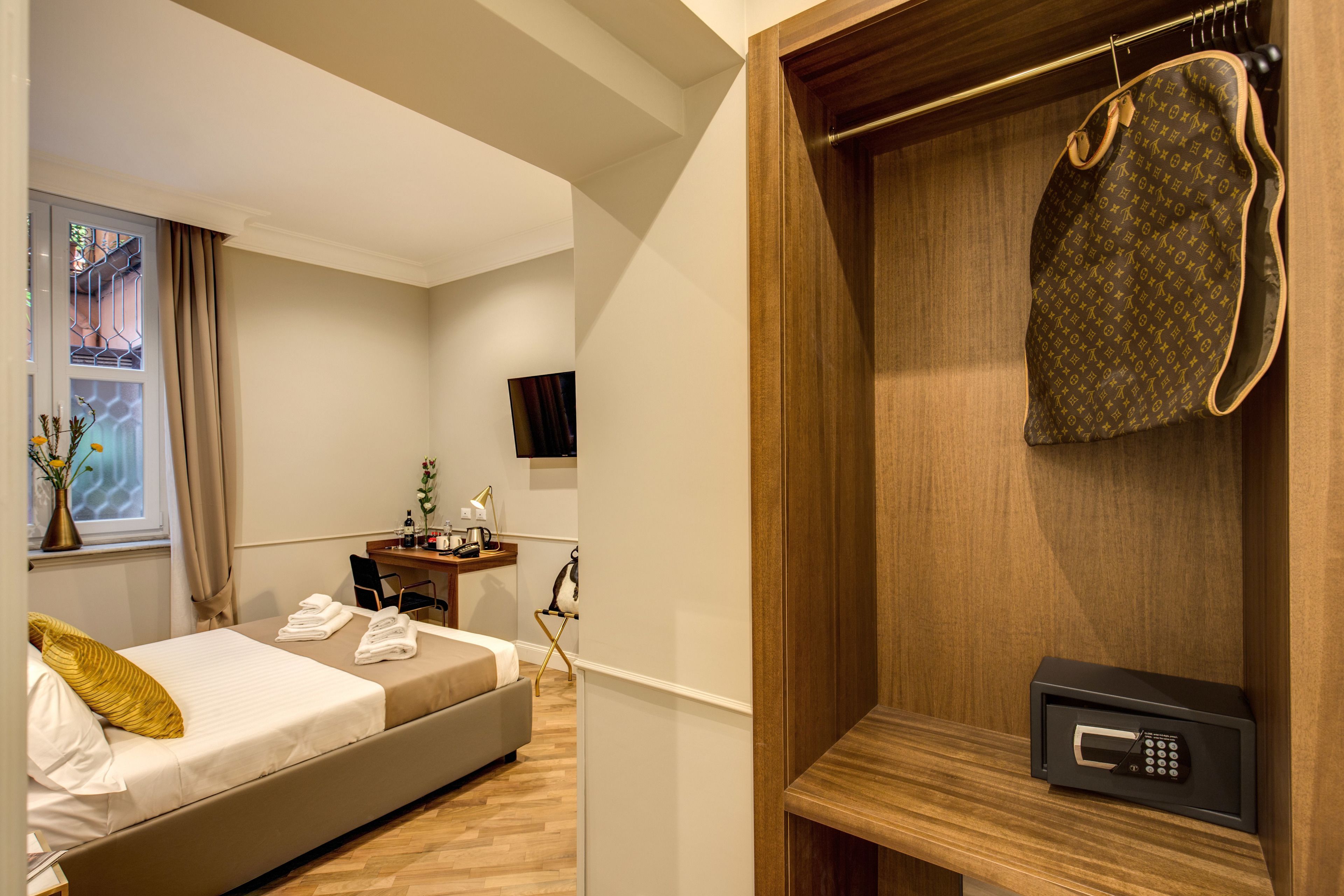 Habitación de hotel con cama, escritorio, televisión, caja fuerte y abrigo colgado en un perchero.