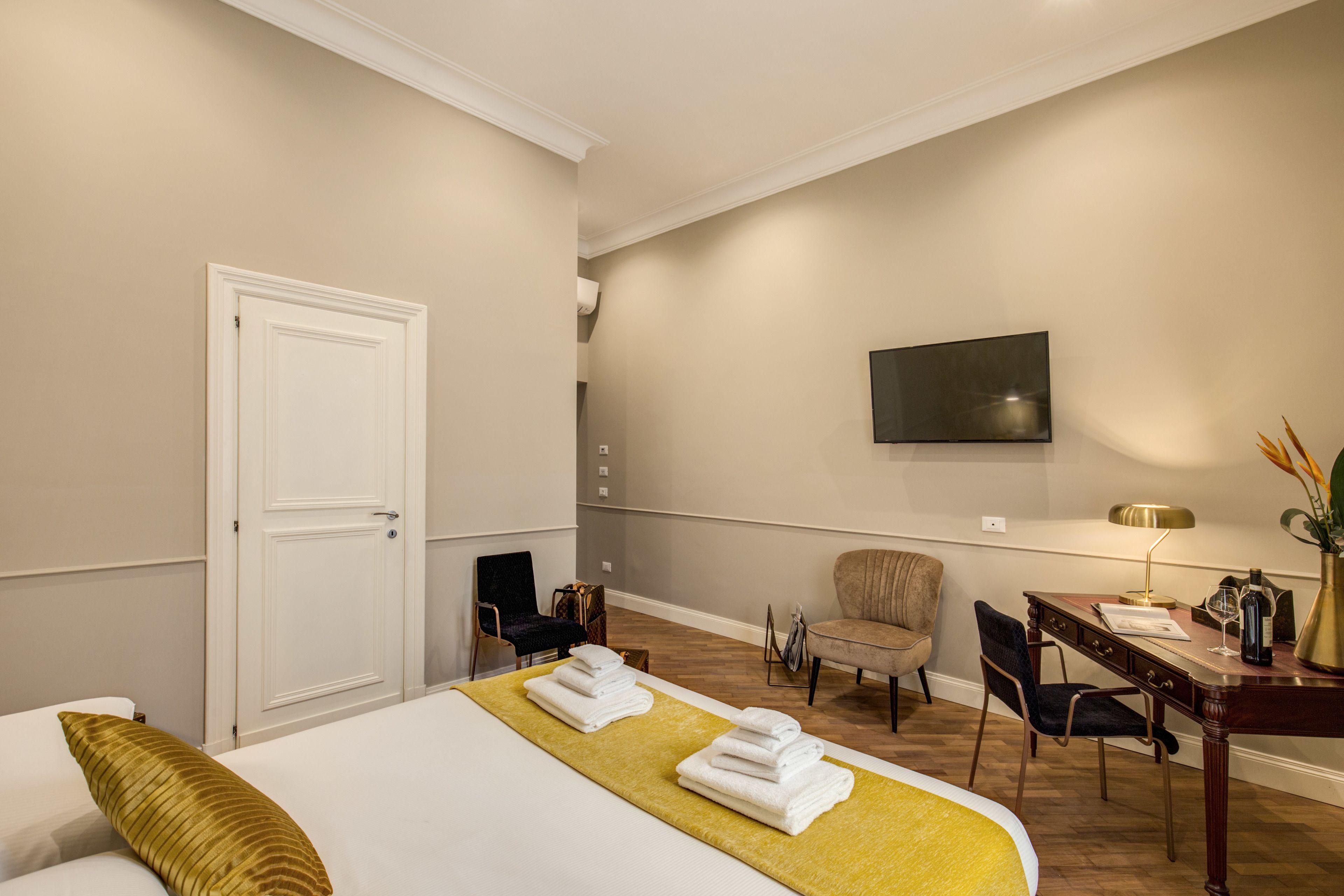 A hotel room with a bed, a desk, a chair, a TV, and a door.