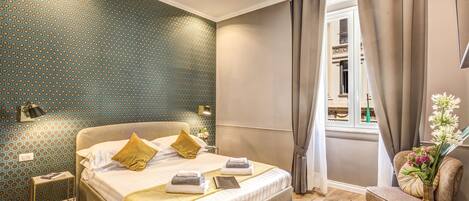 A well-lit bedroom with a large bed, a bedside table, a chair, and a window with curtains.
