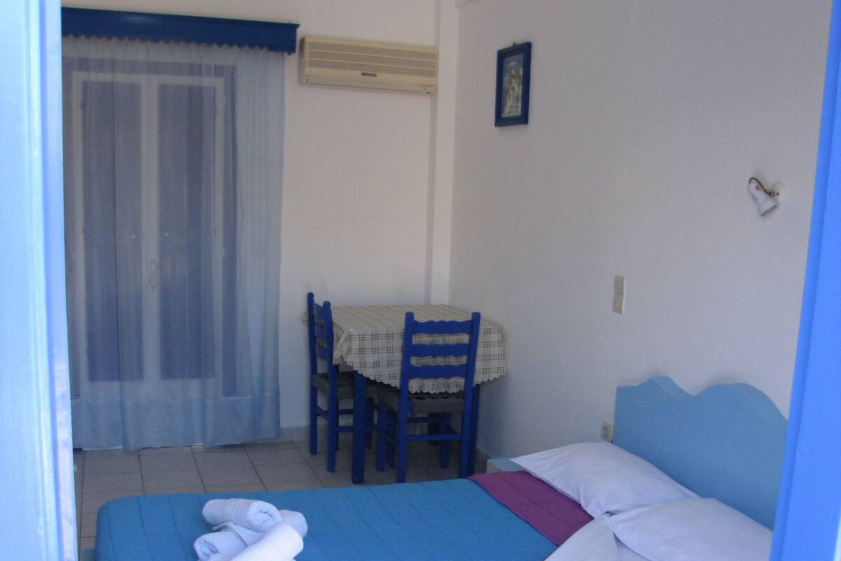 Un dormitorio con una cama, una silla, una mesa y una ventana con cortinas.