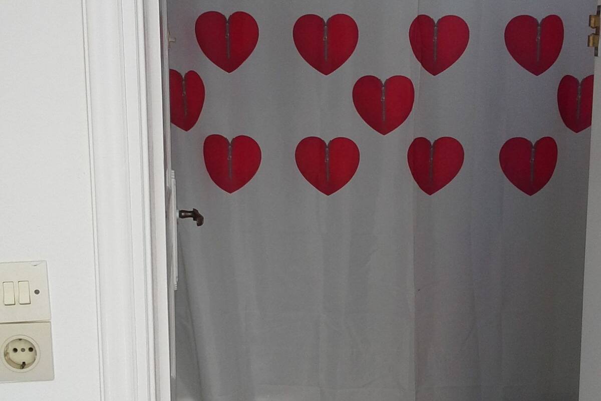 Un baño con inodoro, cortina de ducha con estampado de corazones y una alfombra pequeña en el suelo.